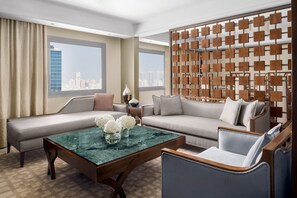 A modern hotel room with a large sofa, a coffee table, and a city view through large windows. - InterContinental Bahrain by IHG (Manama)