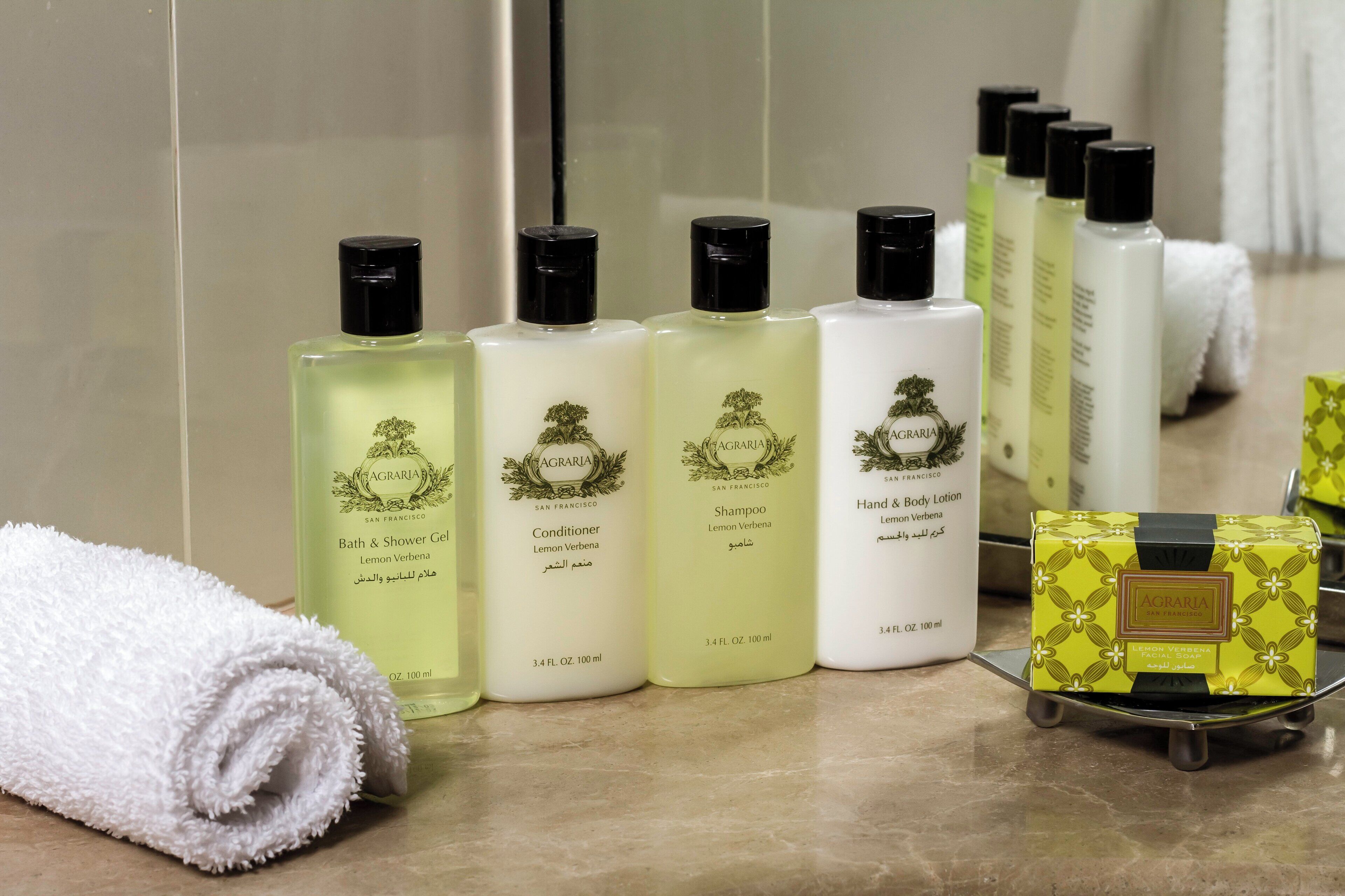 A row of toiletries including a bath towel, bottles of shampoo, conditioner, and hand & body lotion.