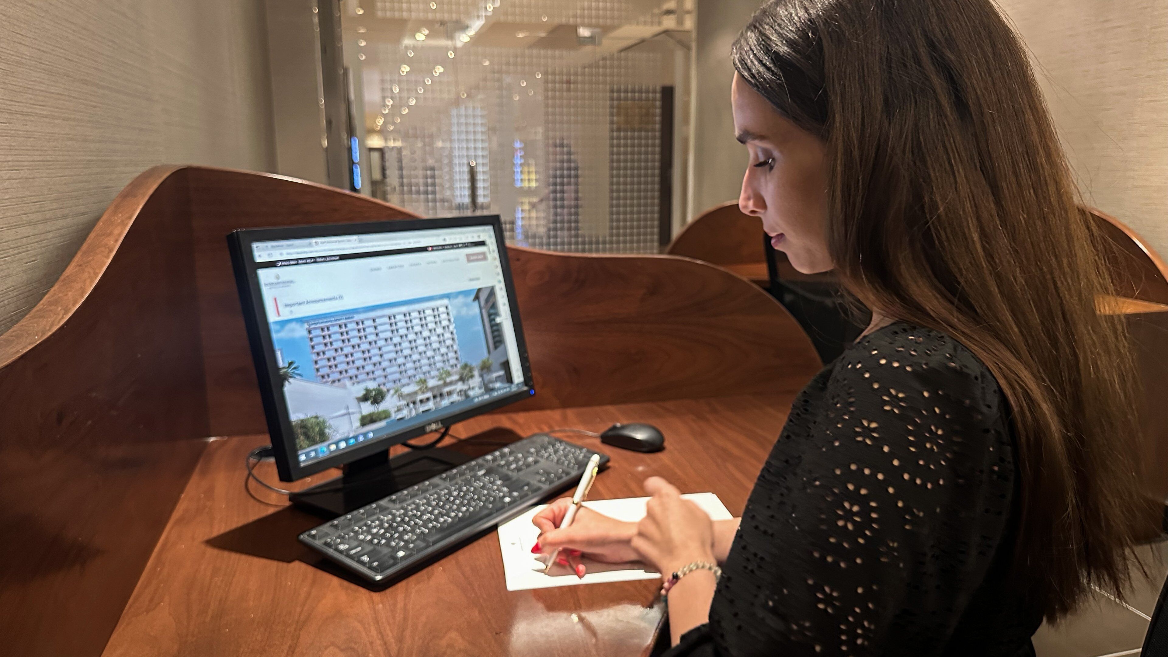 A person at a wooden desk with a computer monitor, keyboard, and mouse.