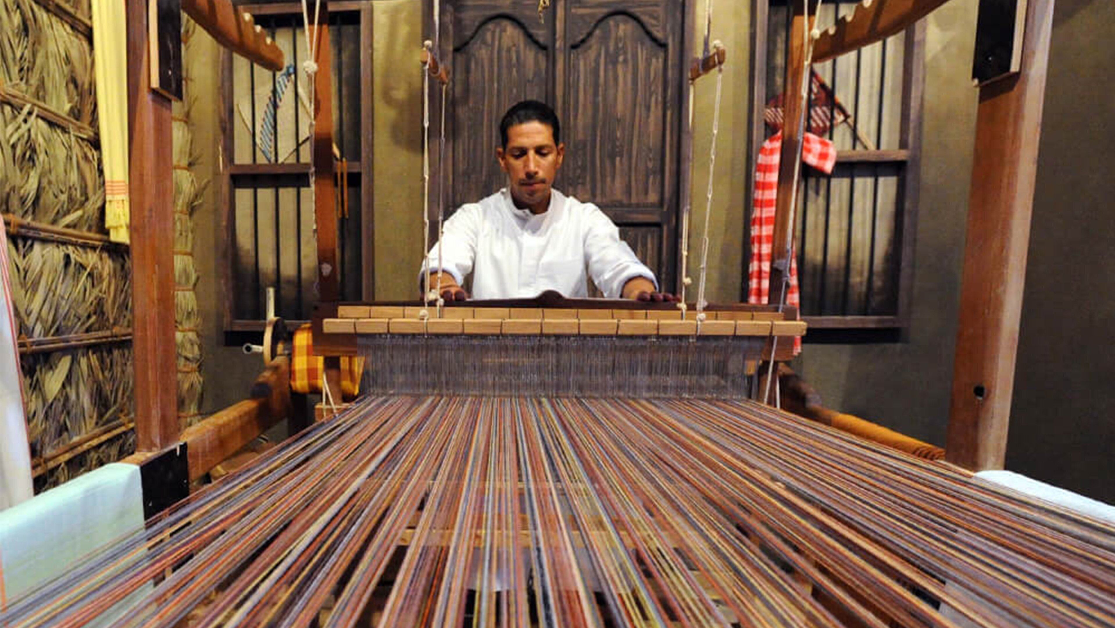 Une personne qui tisse sur un métier à tisser en bois, produisant un tissu à motifs.