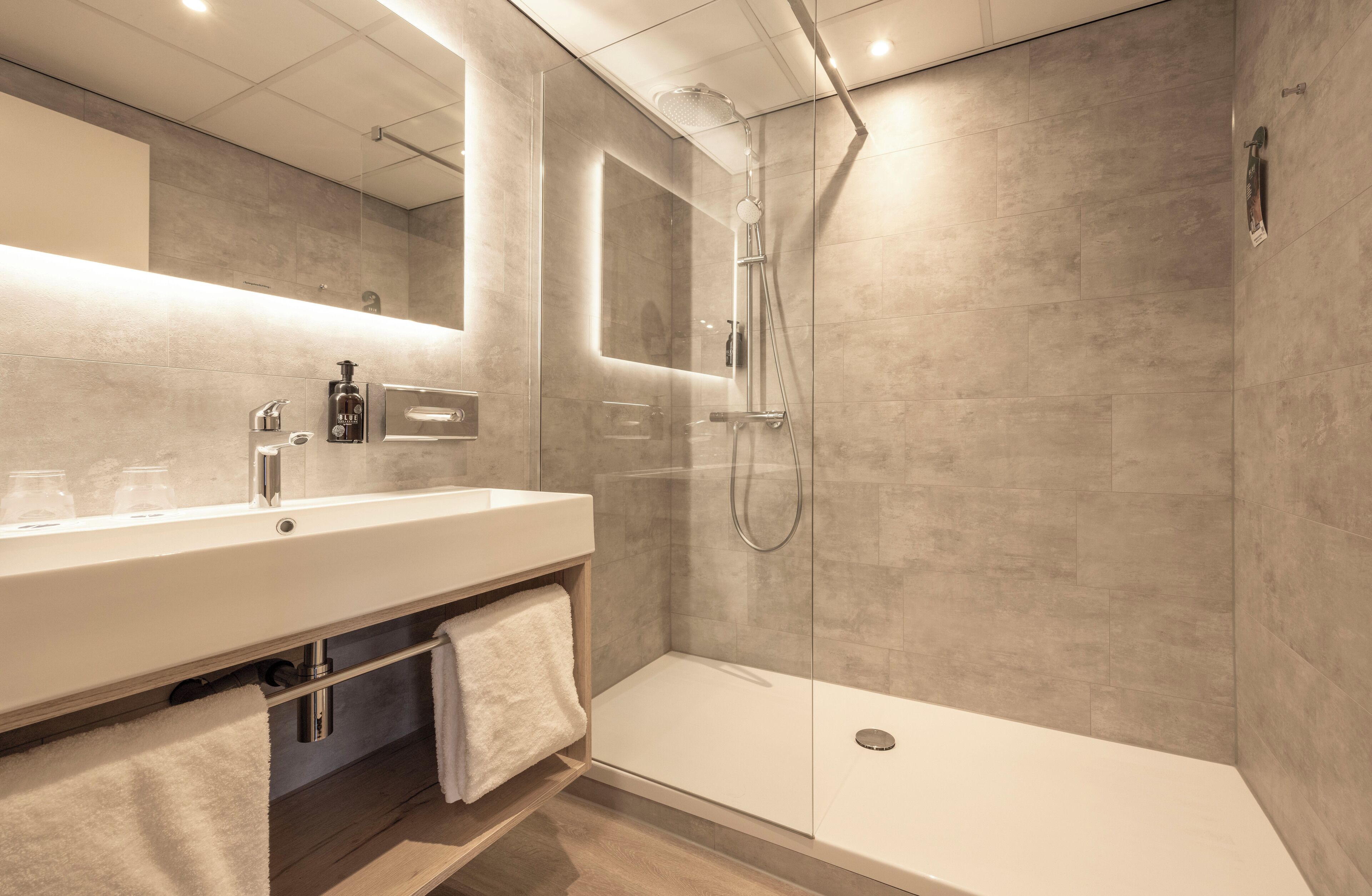A modern bathroom with a glass-enclosed shower, a large mirror, and a white vanity.