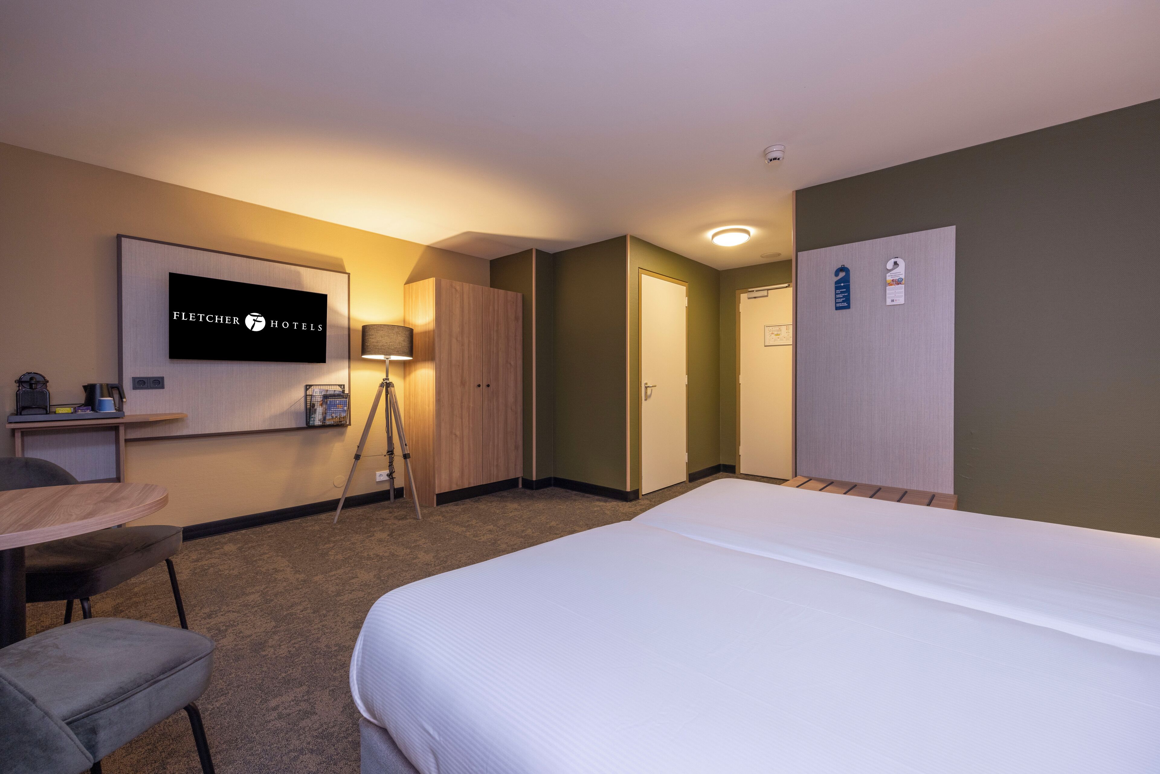 A hotel room with a bed, a desk, a chair, a television, and a wardrobe.