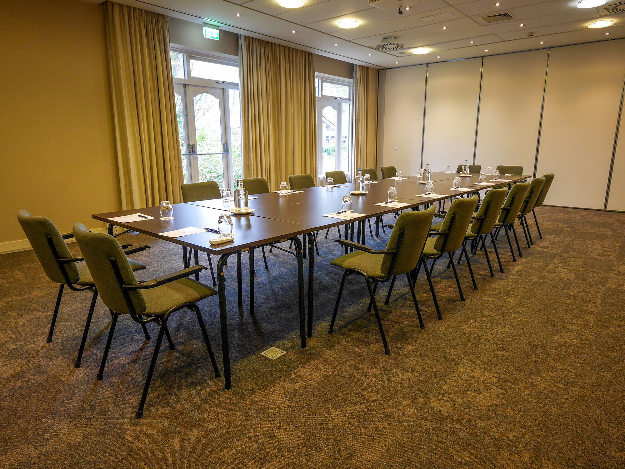 A conference room with a long table, chairs, and windows with curtains.