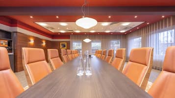 A conference room with a long table and orange chairs, equipped with a ceiling light and windows.