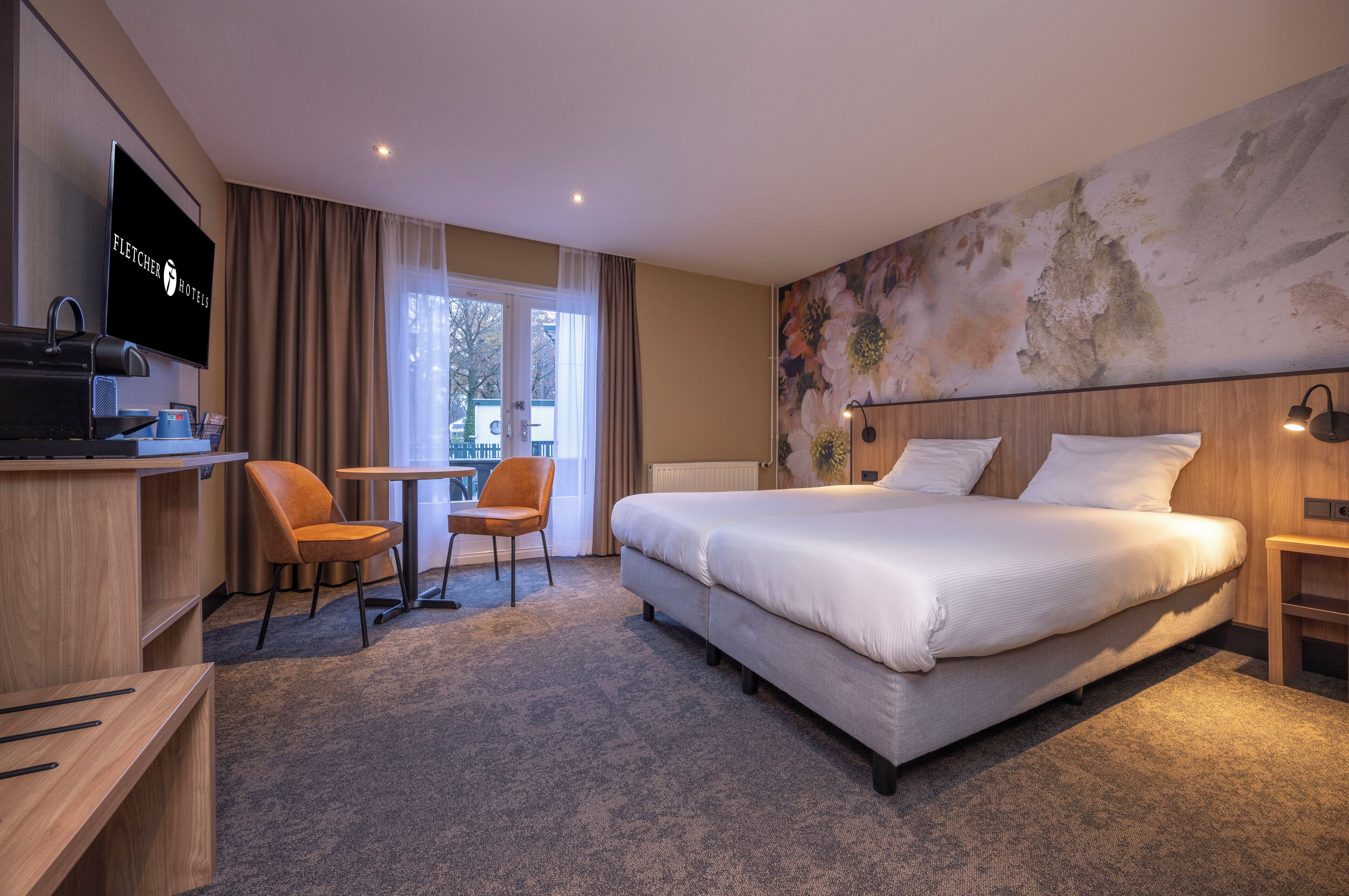 A hotel room with a large bed, a desk with a television, a chair, and a view of the outdoors through a window.