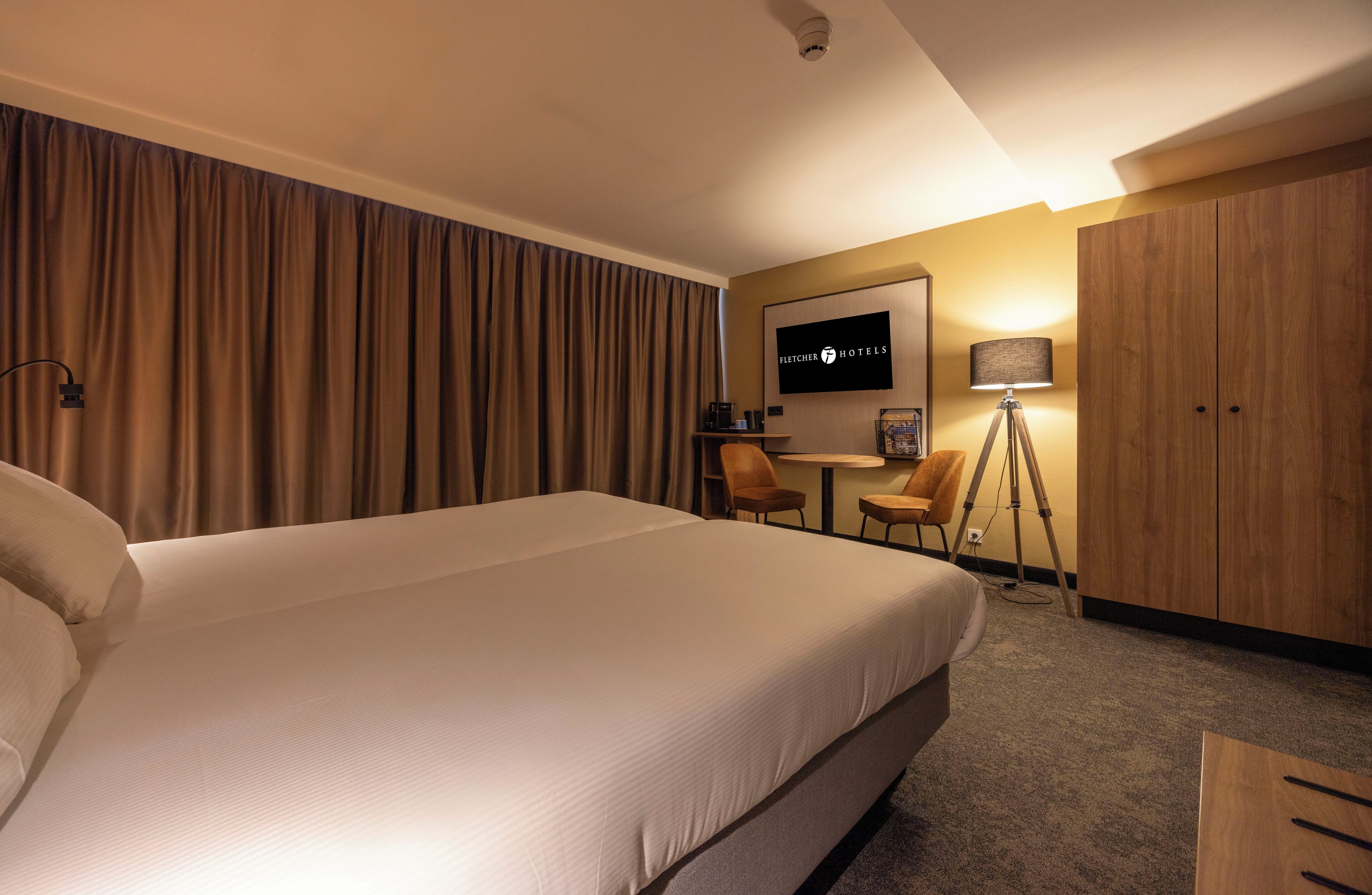 Een hotelkamer met een groot bed, een bureau, een stoel, een televisie en een garderobe.