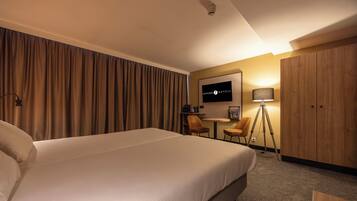Een hotelkamer met een groot bed, een bureau, een stoel, een televisie en een garderobe.