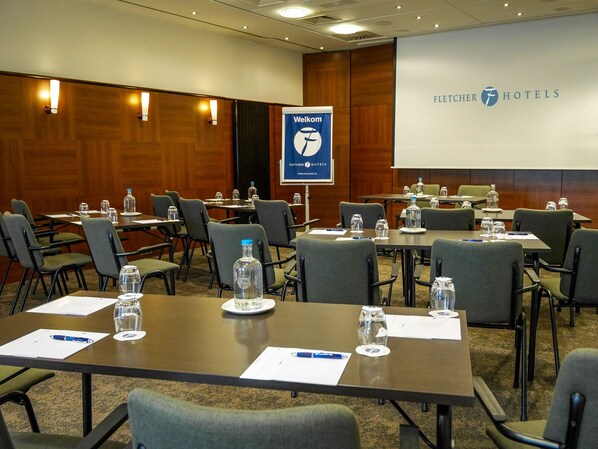 Un salón de conferencias con mesas, sillas, botellas de agua y un cartel de bienvenida en Fletcher Hotels.