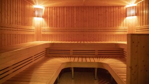 Una sauna de madera con bancos y bancos, techo inclinado y dos luces fijadas a la pared.