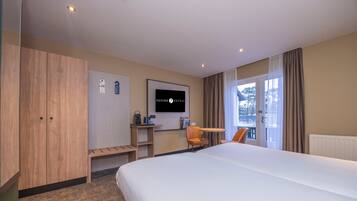 A hotel room with a large bed, wooden wardrobe, a desk with a chair, a television, and a window with curtains.