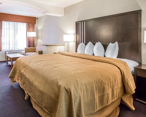 A hotel room with a large bed, a desk, a chair, and a window with curtains.
