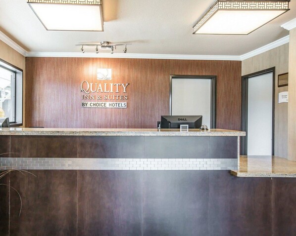 Un mostrador de recepción de hotel con diseño de paneles de madera, una computadora Dell y un letrero que dice "Quality Inn & Suites by Choice Hotels".