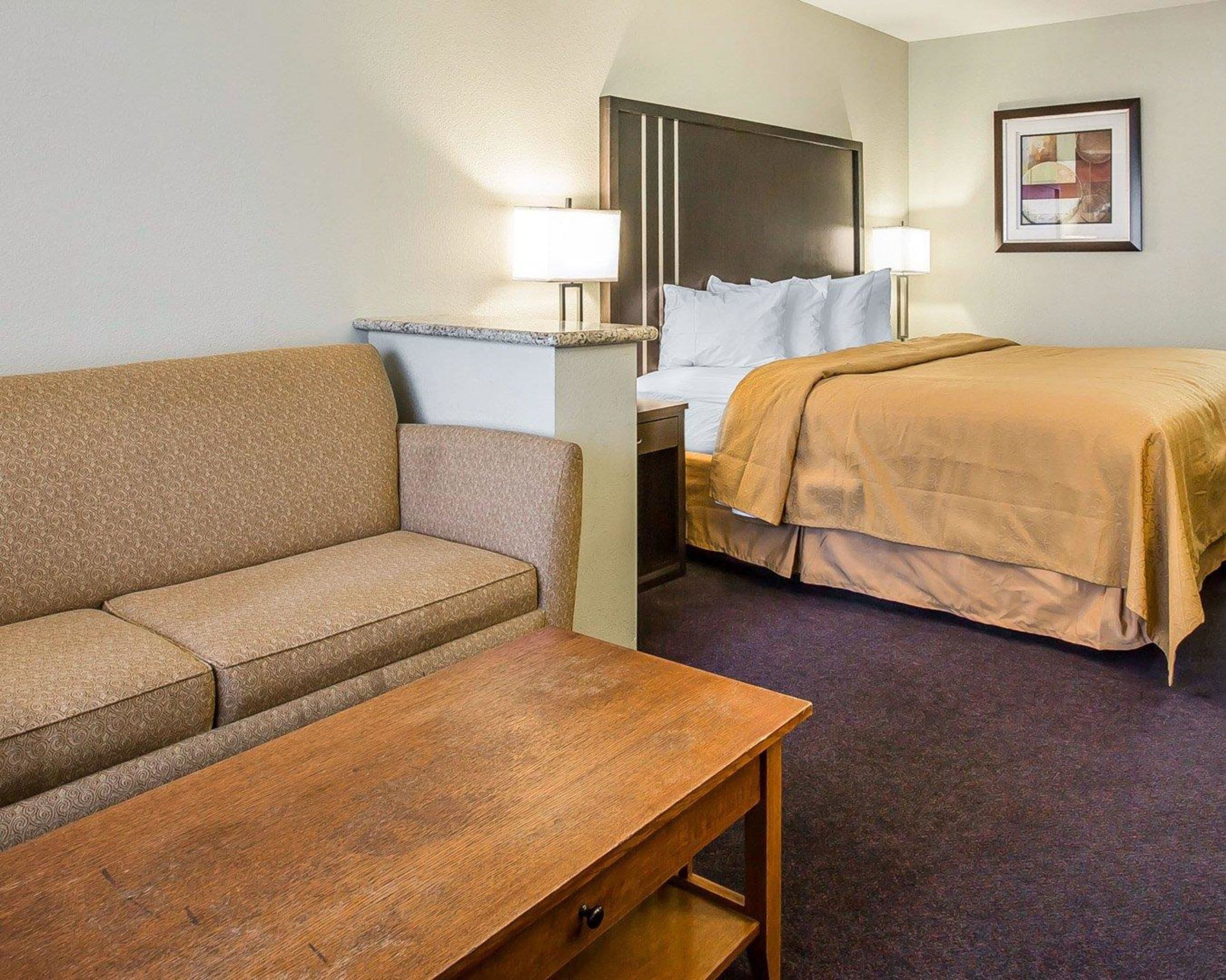 Una habitación de hotel con sofá, cama con cabecera, mesa de madera y dos lámparas de noche.