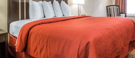 Una habitación de hotel con una cama, una mesita de noche, una lámpara y una silla.