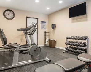 A fitness center with cardio equipment, dumbbells, and a wall clock.