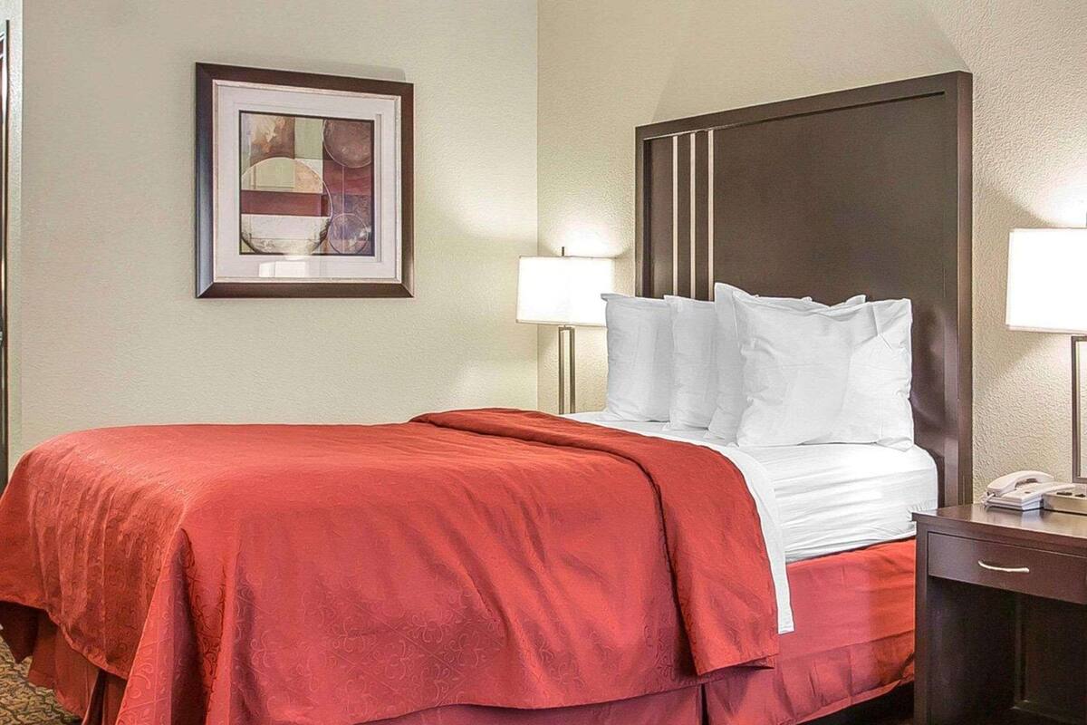 A hotel room with a bed, two bedside lamps, a framed picture on the wall, and a telephone on the nightstand.