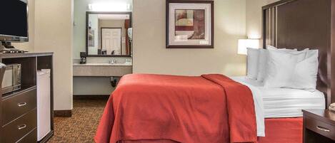 A hotel room with a bed, a desk, a television, a mirror, and a bathroom visible through an open door.