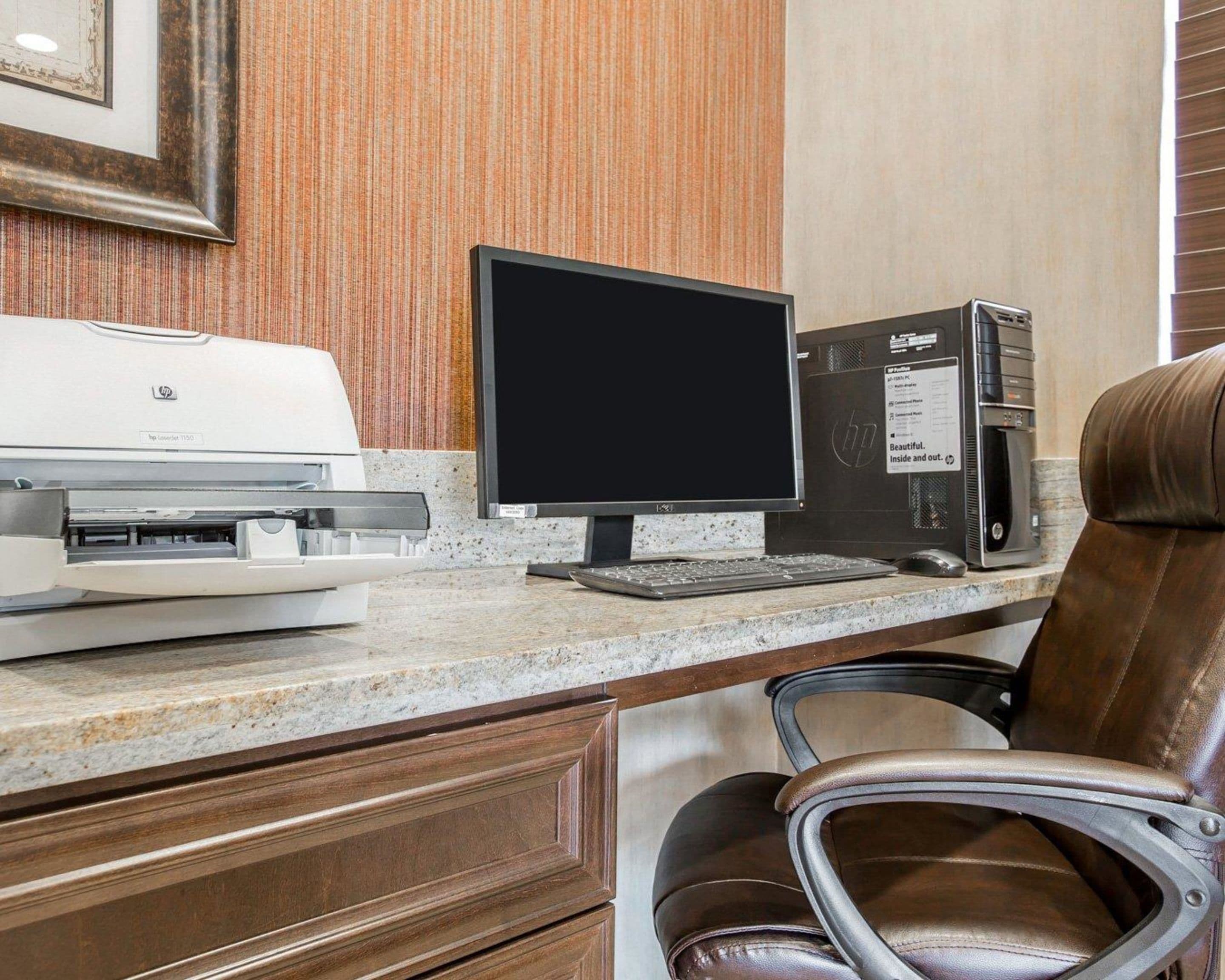 A hotel workspace with a desktop computer, printer, and leather chair.