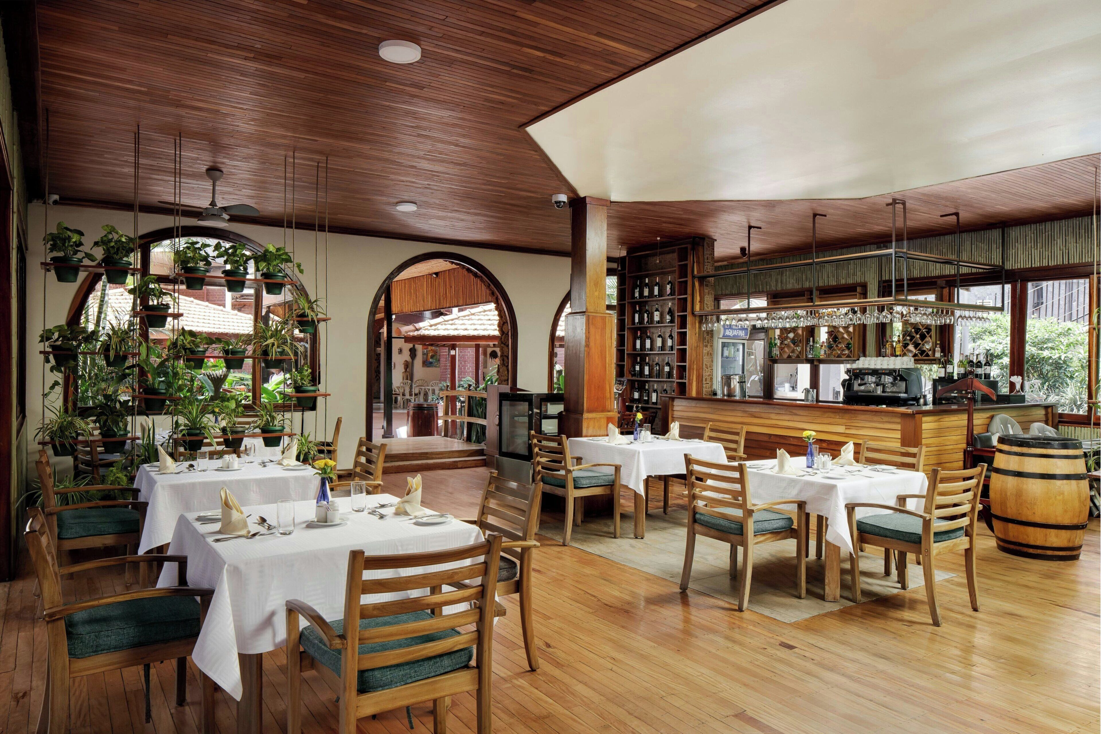 A restaurant with wooden furniture, white tablecloths, and a bar area.