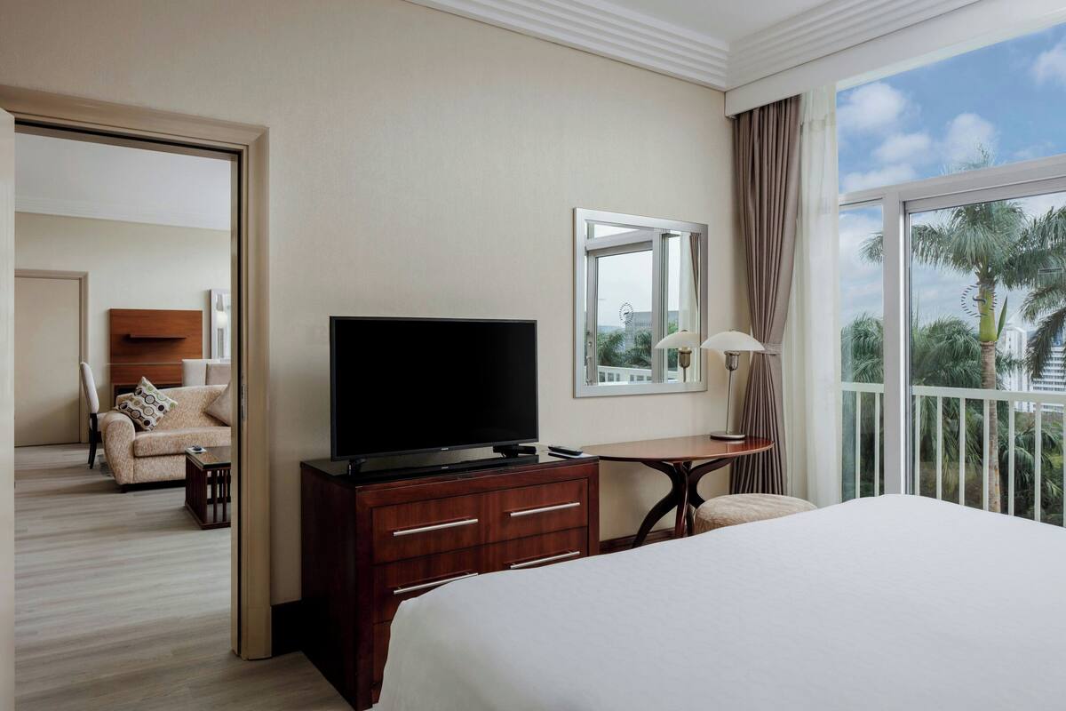 A hotel room with a bed, a TV, a desk, a chair, and a balcony with a view.