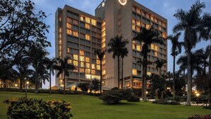 A multi-story hotel with a prominent logo on the corner, surrounded by well-maintained lawns and palm trees. - Sheraton Kampala Hotel (Kampala)