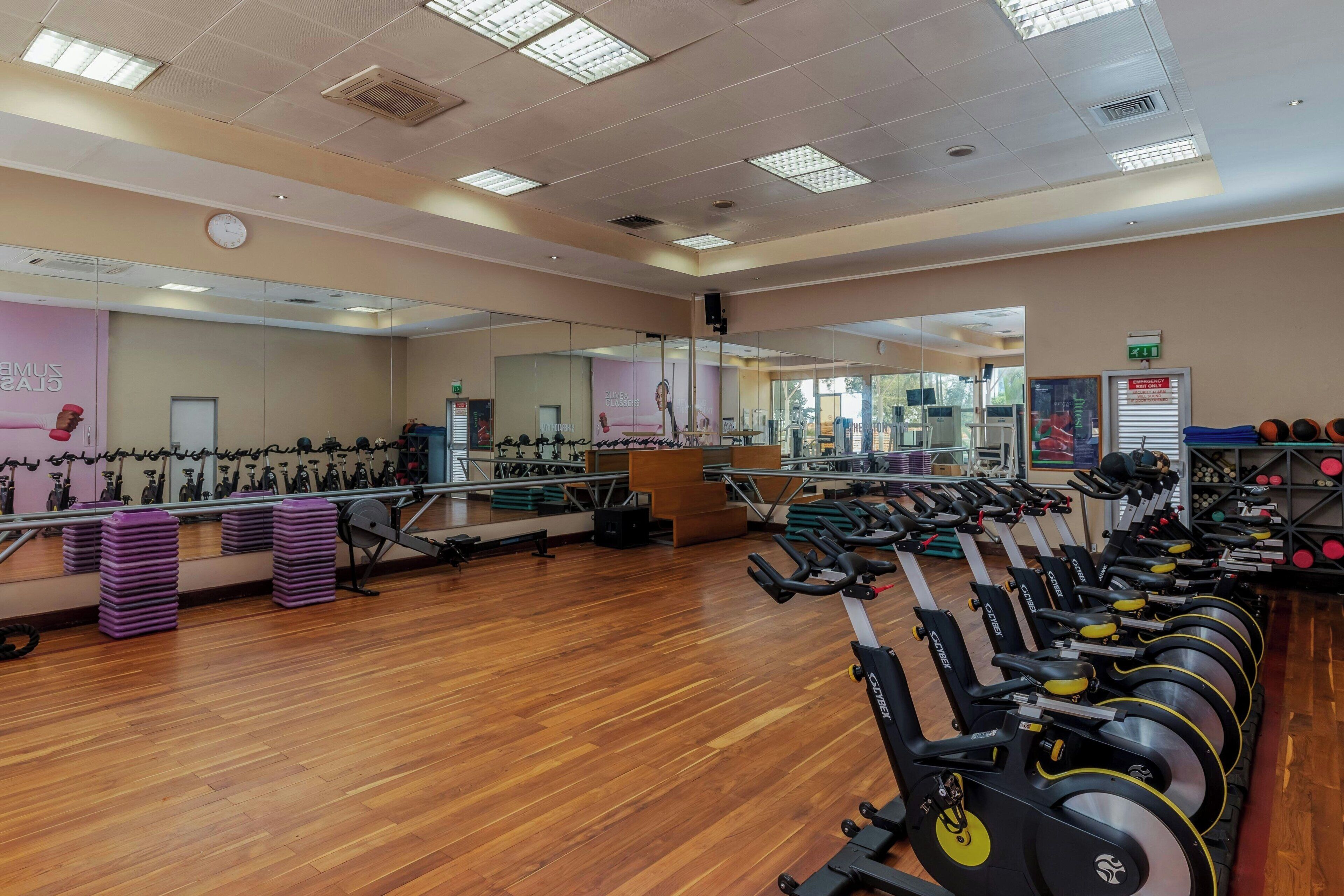 Ein Fitnessraum mit Trainingsgeräten, Spiegeln und Holzboden.