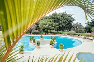 Una piscina circular con sillas de descanso y sombrillas, rodeada de exuberante vegetación y árboles.