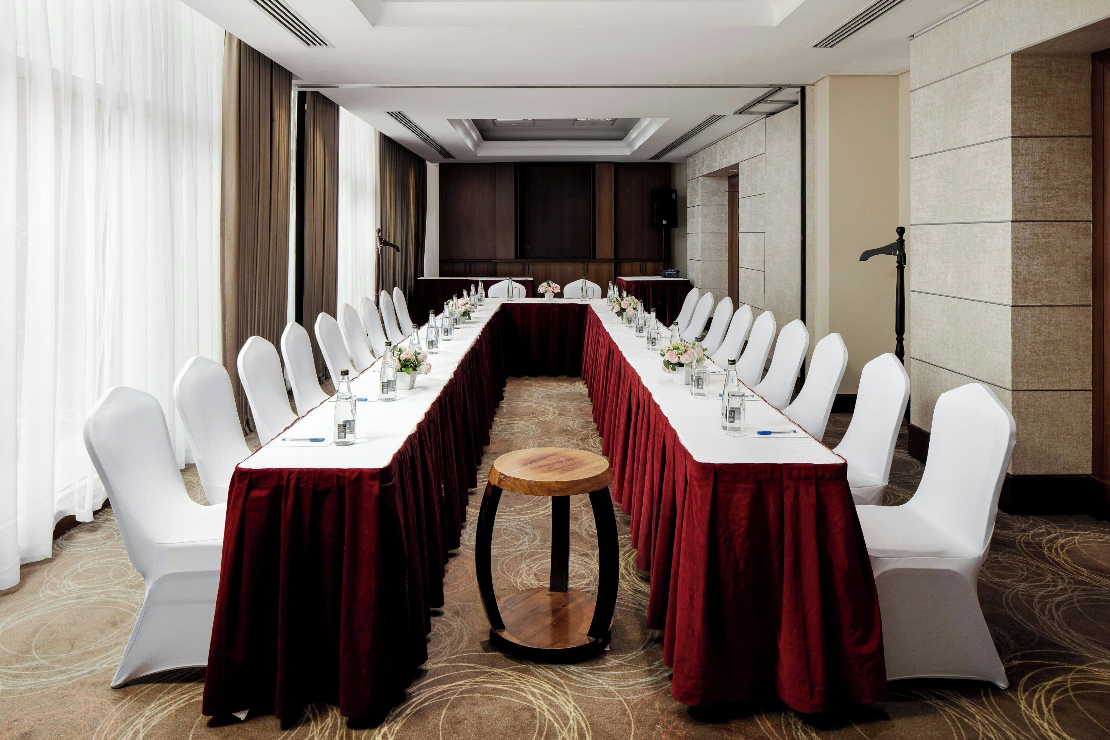 Une salle de conférence avec une longue table, des chaises blanches et un tabouret en bois.