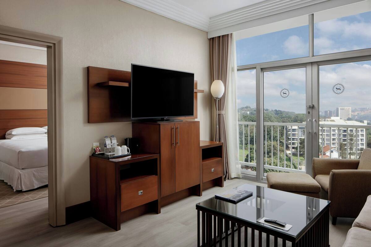A hotel room with a bed, a TV, a coffee table, a sofa, and a balcony with a city view.