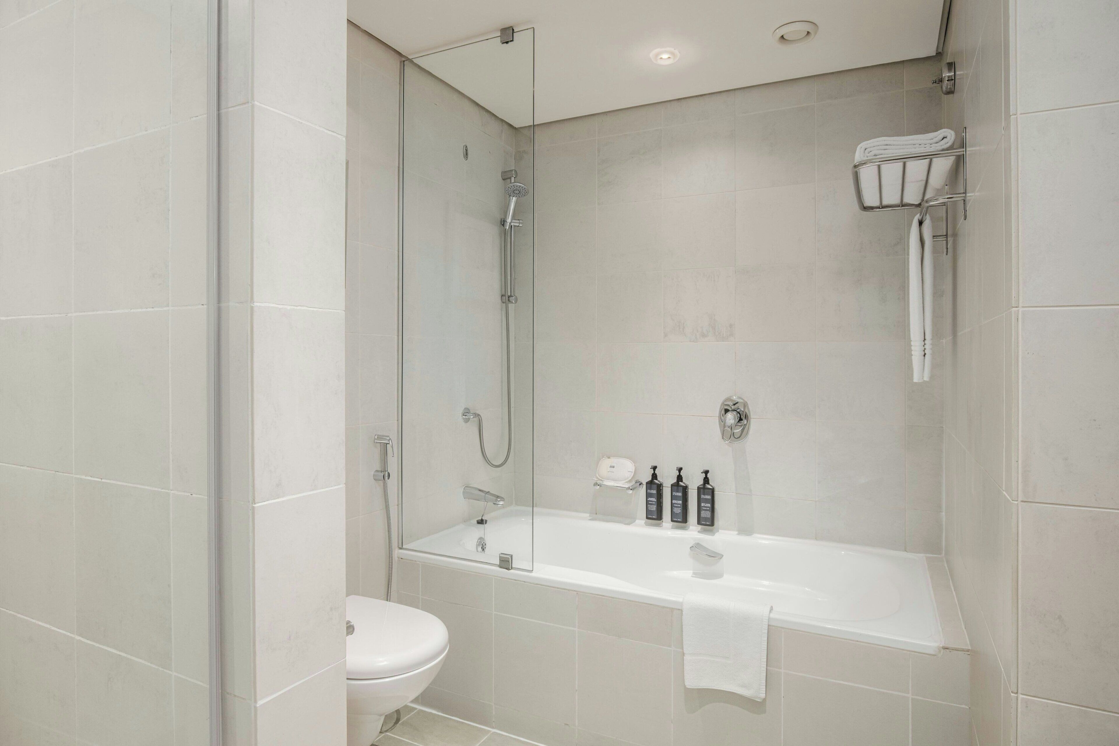 A modern bathroom with a glass-enclosed shower, a white bathtub, and a toilet.