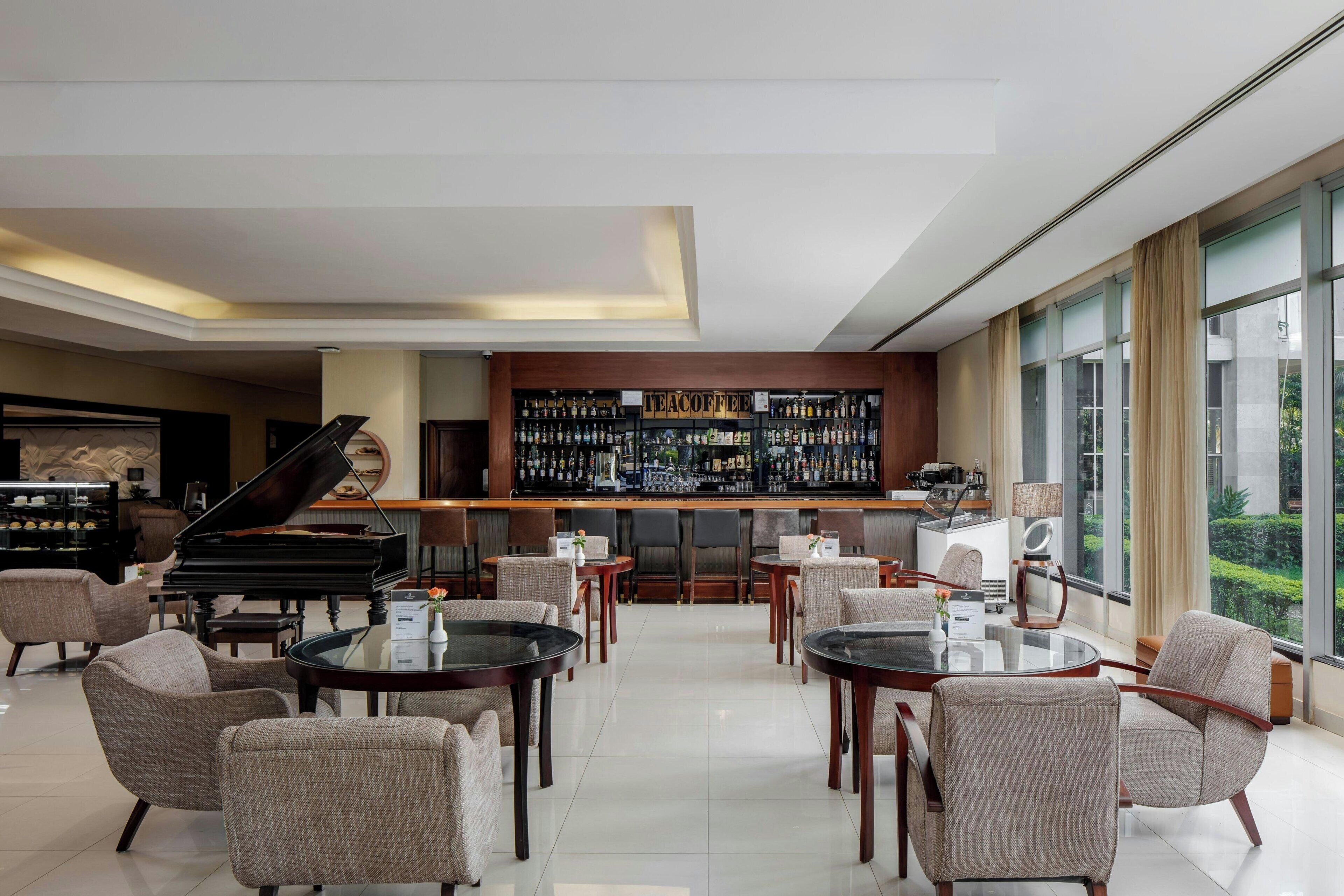 A modern bar area with a piano, seating, and a view of greenery.