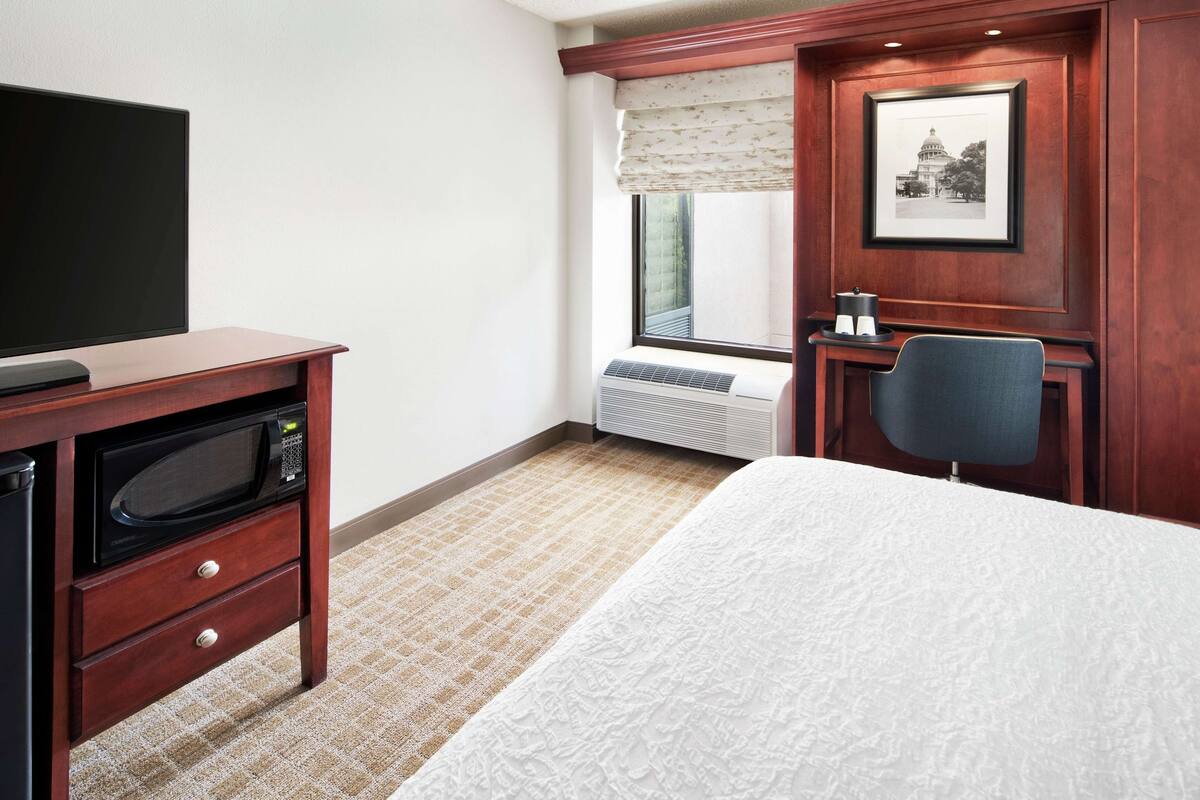Ein Hotelzimmer mit Bett, Schreibtisch mit Mikrowelle, Stuhl, Heizkörper und einem gerahmten Bild an der Wand.