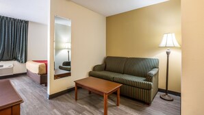 A hotel room with a sofa, a small table, a lamp, a mirror, and a window with curtains. - Econo Lodge Inn & Suites Fairview Heights - St. Louis (Fairview Heights)
