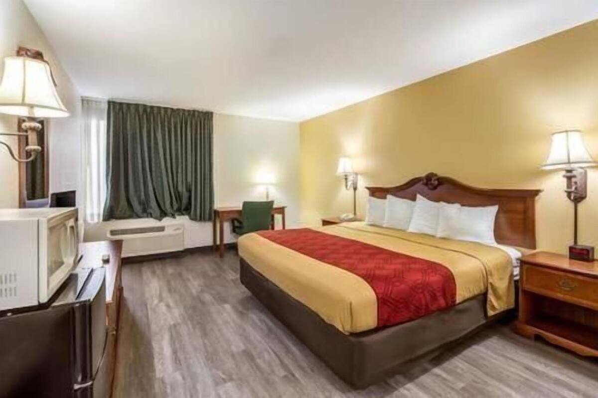 A hotel room with a bed, bedside lamps, a desk, a chair, and a window with curtains.