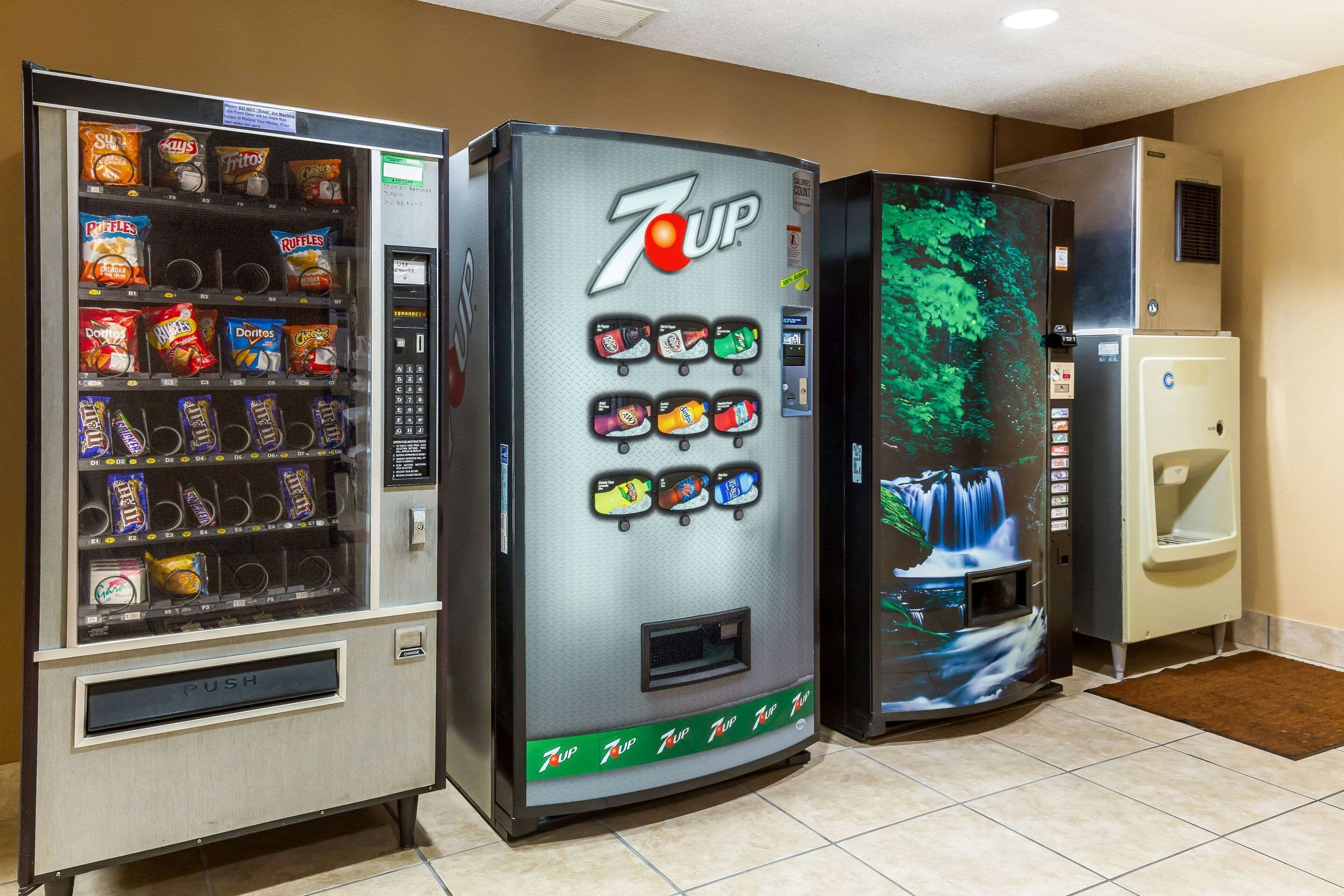 Drei Getränkeautomaten mit Snacks und Getränken, darunter 7UP, in einem Raum mit gefliestem Boden.