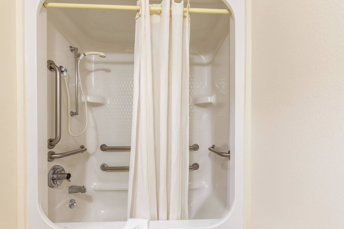 A bathtub with a showerhead, grab bars, and a curtain.