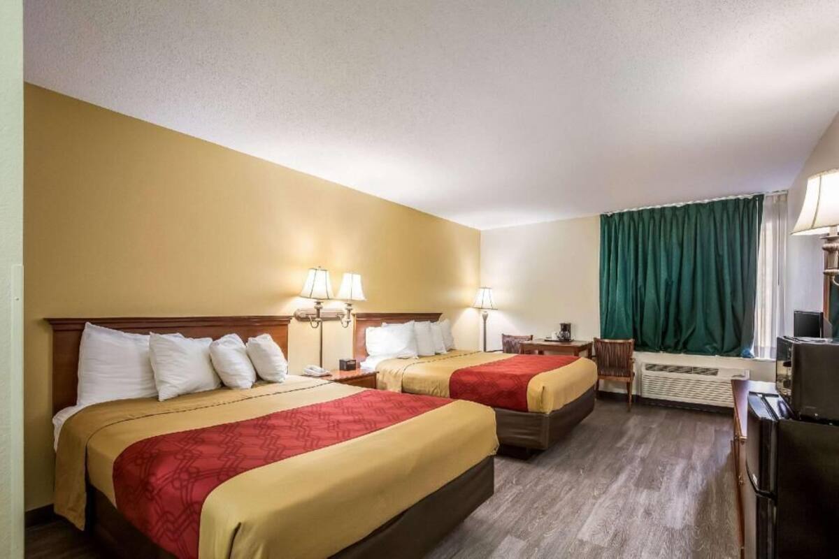 A hotel room with two beds, a desk, a television, and an air conditioning unit.