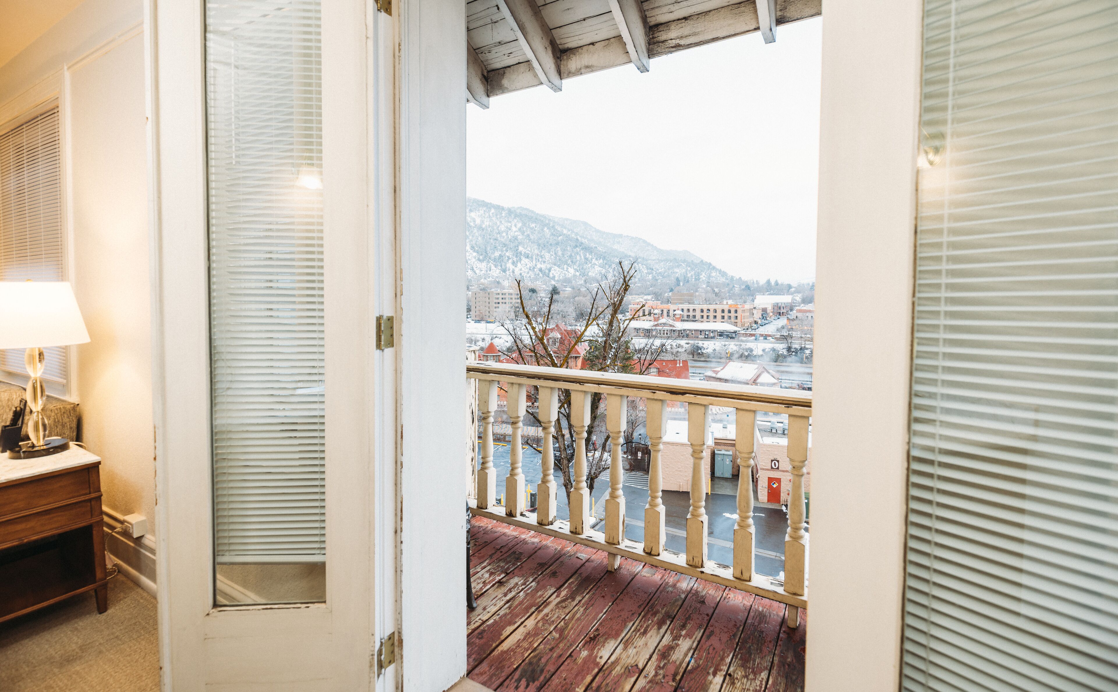 Eine offene Tür, die auf einen Balkon mit Blick auf eine verschneite Landschaft und Gebäude führt.