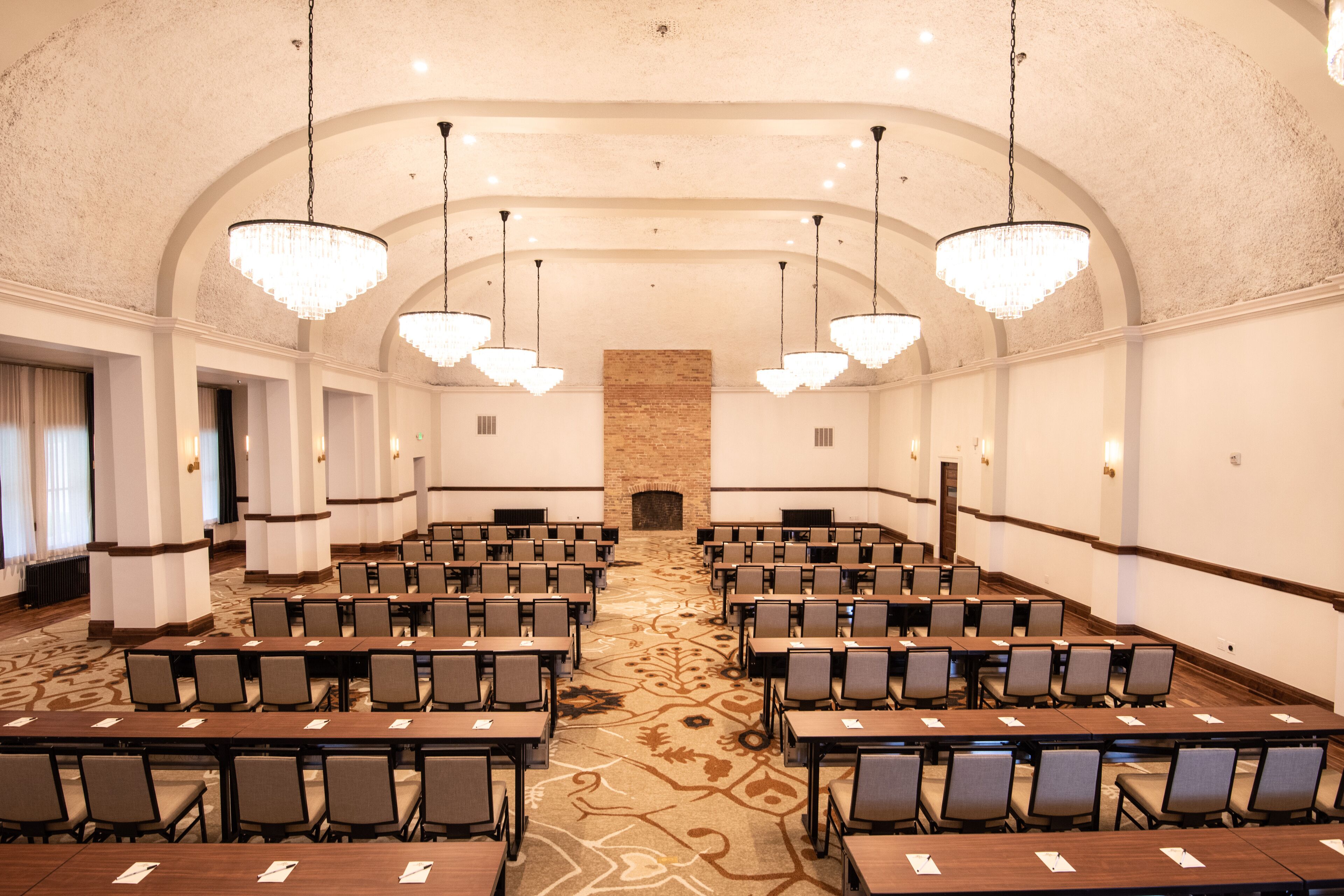 Une salle de conférence avec des rangées de tables et de chaises, de grands lustres et une cheminée en pierre.