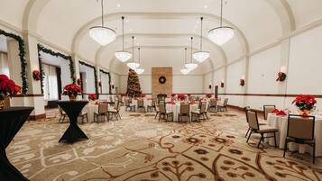 Una gran sala de banquet decorada amb elegància, amb alts sostres, lluminàries penjants i un arbre de Nadal al centre. Les taules tenen estovat blanc i elements decoratius vermells.