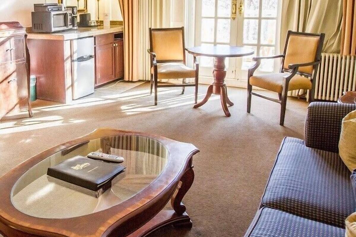 A hotel room with a dining area, a sofa, a glass coffee table, and a view of the outdoors through large windows.