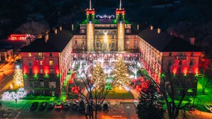 A historic building with a central tower and two smaller towers, surrounded by trees and illuminated by colorful lights. - Hotel Colorado (Glenwood Springs)