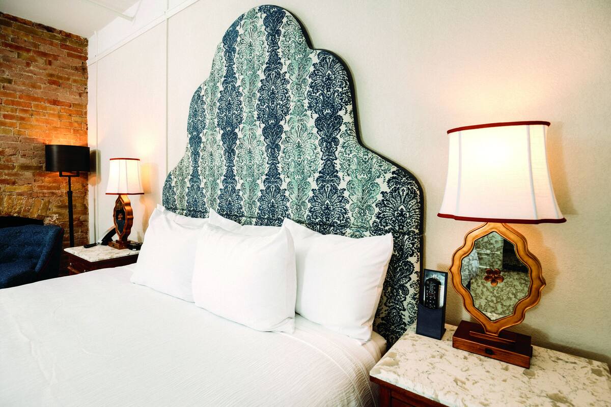 A neatly made bed with white linens, a patterned headboard, and two bedside lamps.