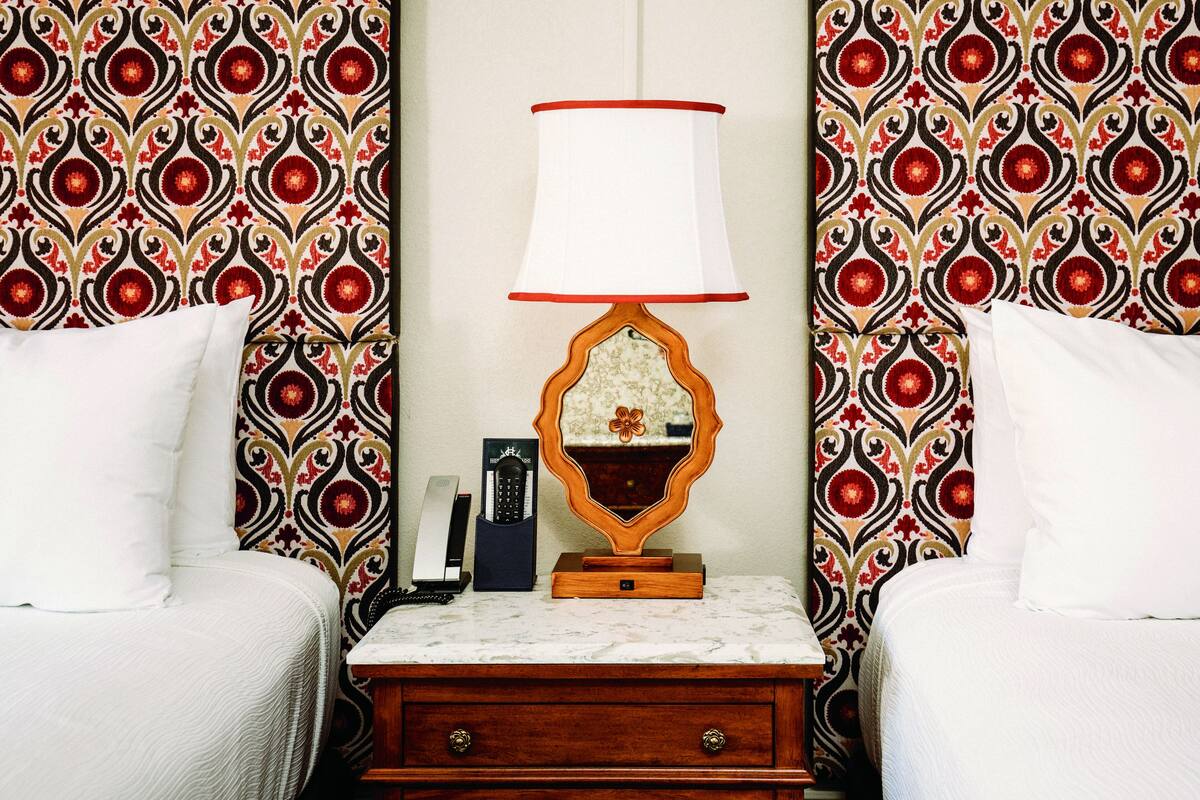 A hotel room with a bed, a nightstand with a lamp, a telephone, and a decorative mirror.