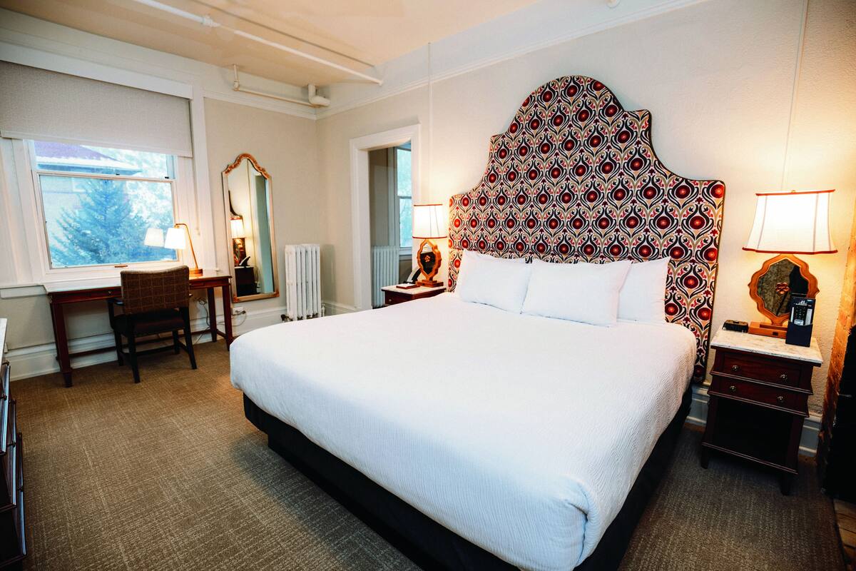 A hotel room with a large bed, a desk, a chair, a nightstand, and a mirror.