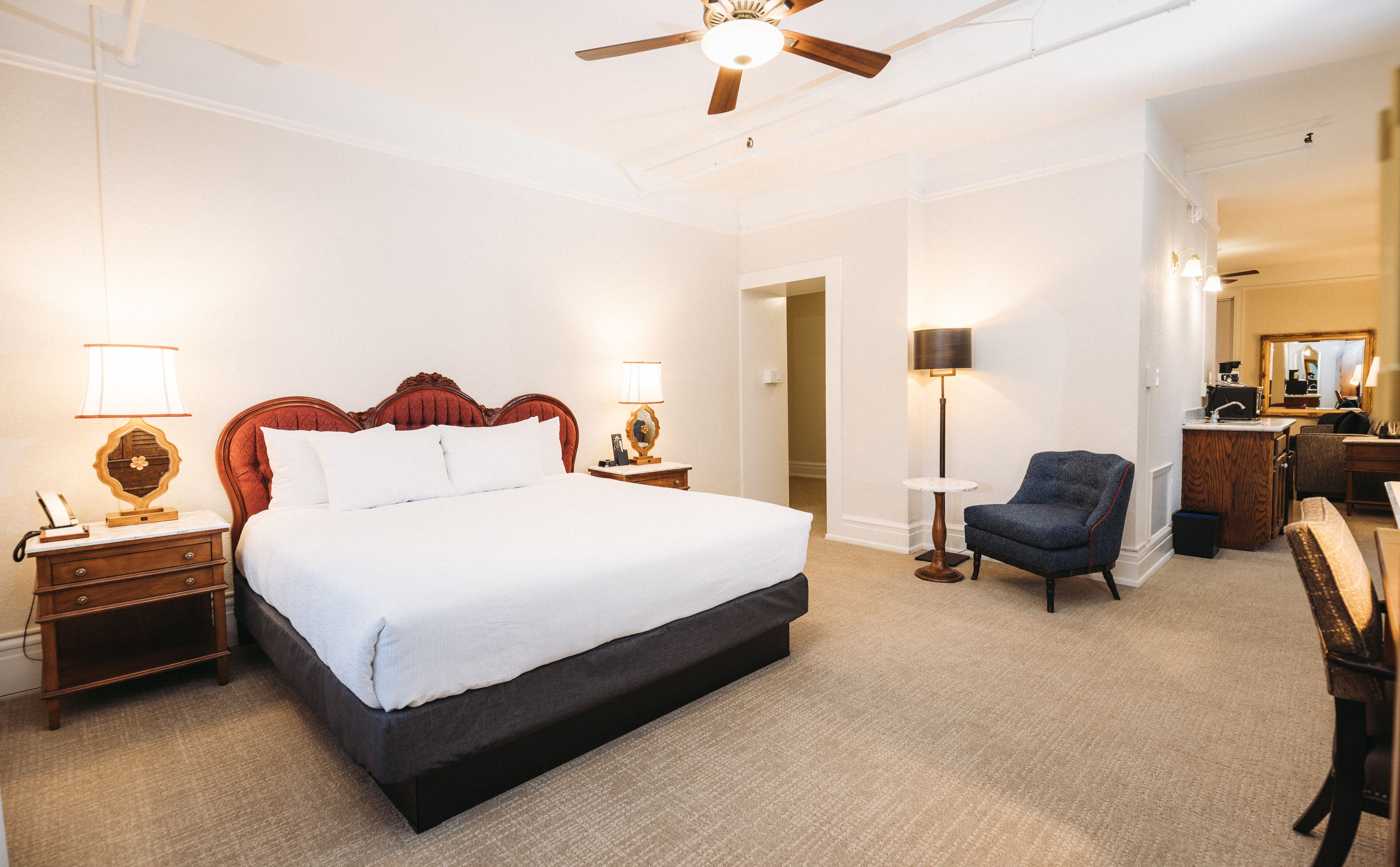 Une chambre d’hôtel avec un grand lit, des tables de chevet, une lampe de chevet, une chaise et un bureau avec un miroir.