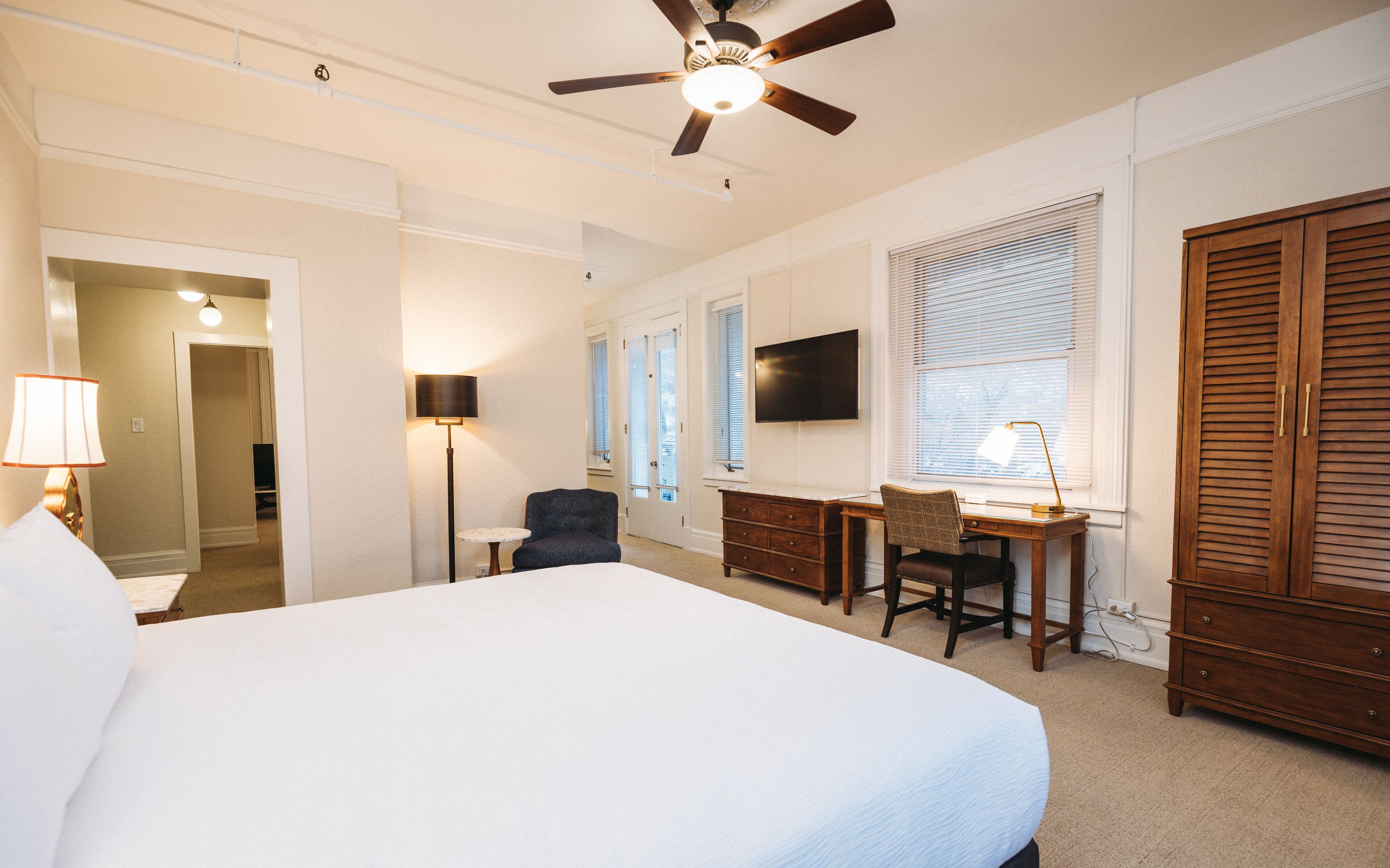 A hotel room with a large bed, a desk with a chair, a television, and a wardrobe.
