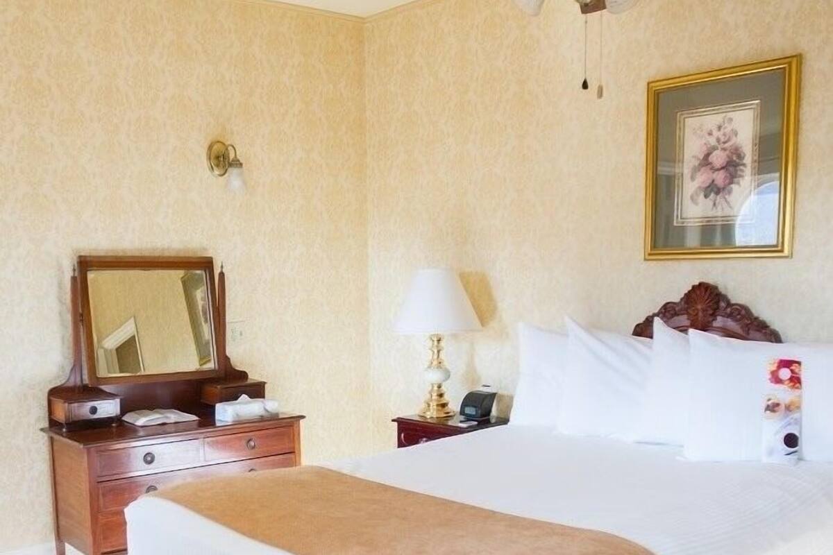 A hotel room with a large bed, a bedside table with a lamp, a mirror, and a framed picture on the wall.