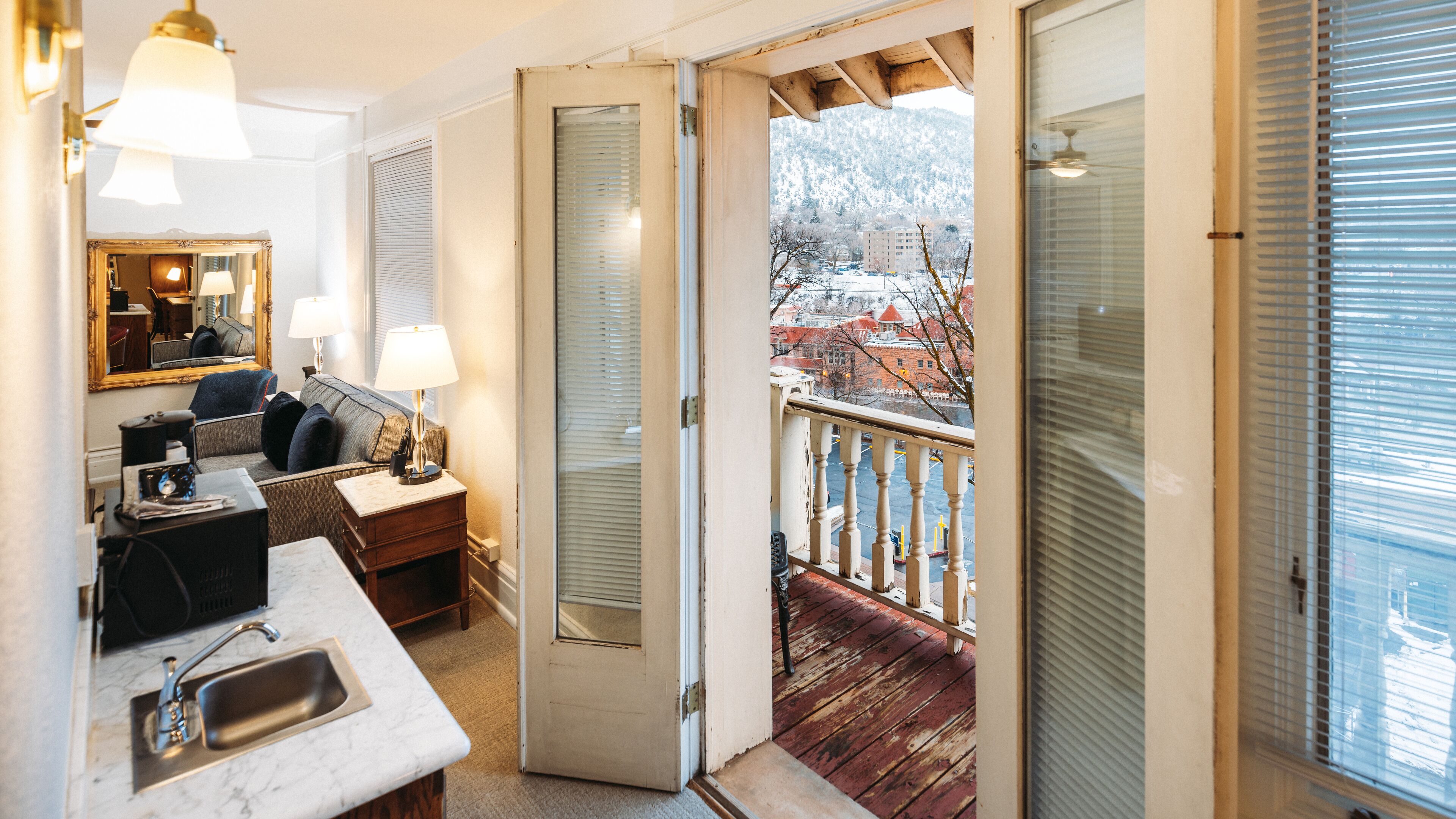 Una habitación acogedora con sofá, una mesita, un espejo y un balcón con vistas a un paisaje nevado.