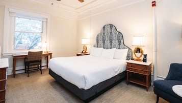 Een hotelkamer met een groot bed, twee nachtkastjes met lampen, een bureau, een stoel en uitzicht op bomen door het raam.
